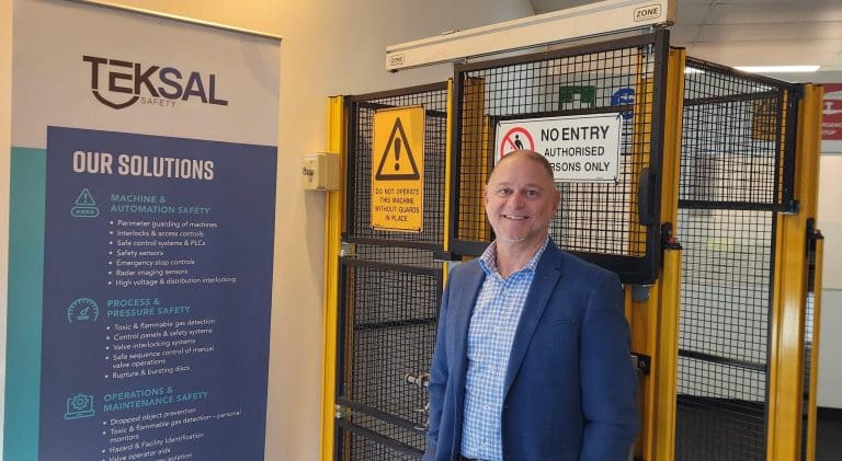 Managing Director of Teksal standing in front of machine guarding and a company promo banner.