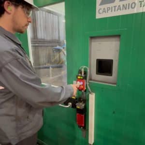 Worker pressing blue pushbutton on a Fortress interlock system mounted to a green machine enclosure.