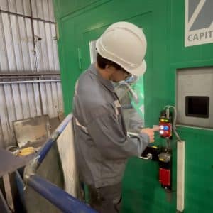 Worker pressing pushbutton on a Fortress interlock system mounted to a green machine enclosure.