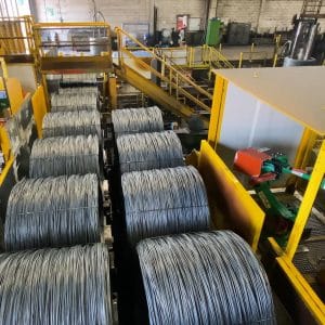 Steel wire coils on production line with yellow guarding and safety interlocks in an industrial facility.