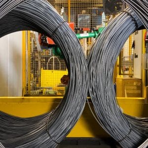Large steel wire coils with yellow safety guarding in the background.